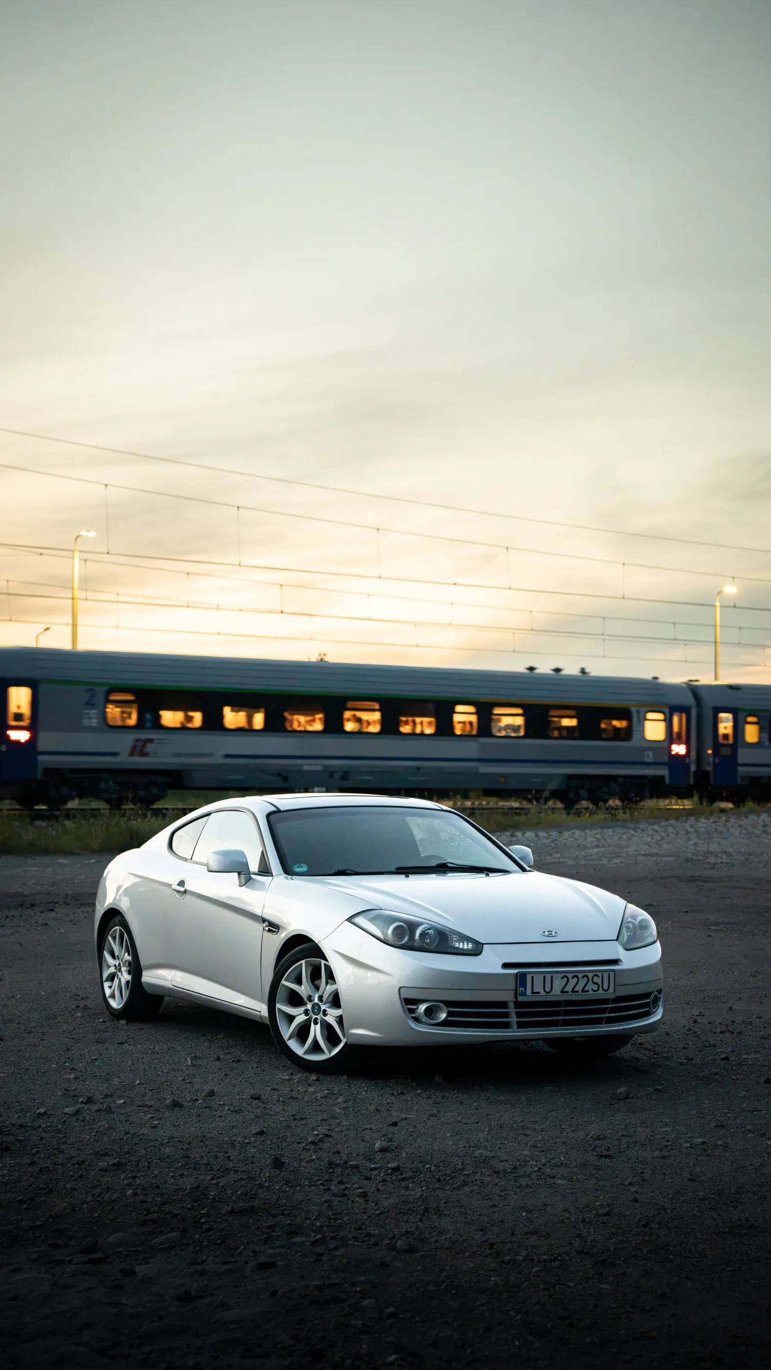Srebrny Hyundai Coupe na tle pociągu o zachodzie słońca